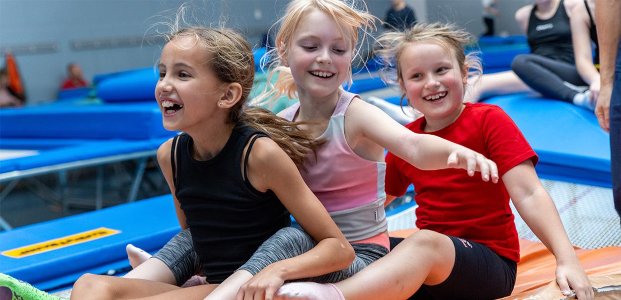 Tre piger sidder på en trampolin og griner
