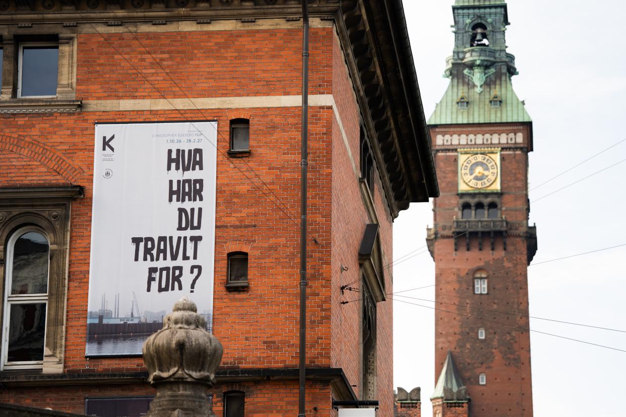 Udstillingsplakat med teksten HVA' HAR DU TRAVLT FOR? på Københavns Museums facade. Rådhustårnet i baggrunden