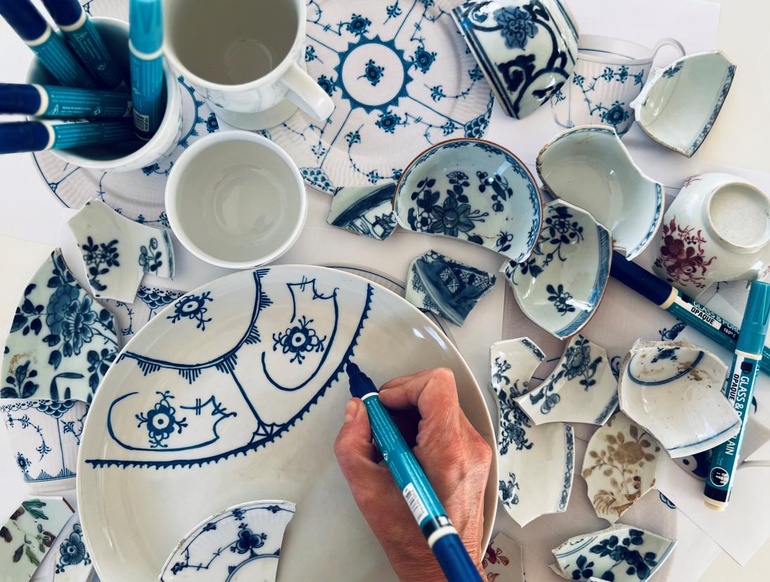 Hånd, der dekorerer hvidt porcelæn med blå tusch-maling.